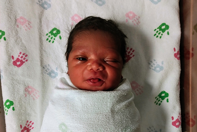Newborn baby, Donyell, swaddled in a blanket and winking at the camera