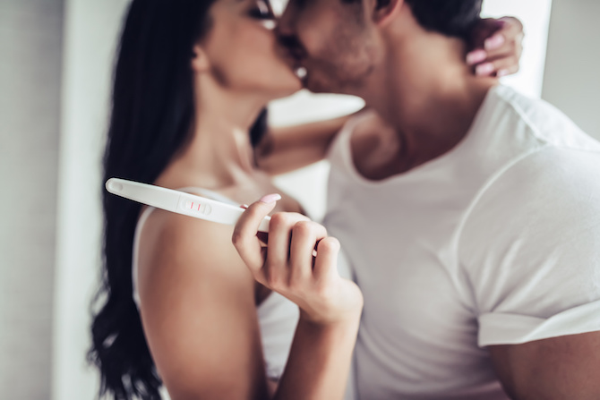 Couple kissing while holding a positive pregnancy test