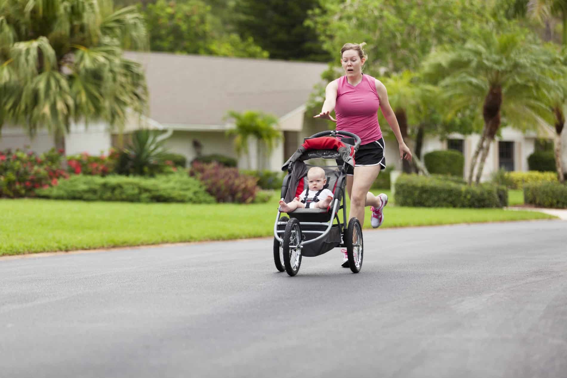A worried woman running behind a baby's stroller on the street reaches for the stroller's handlebars