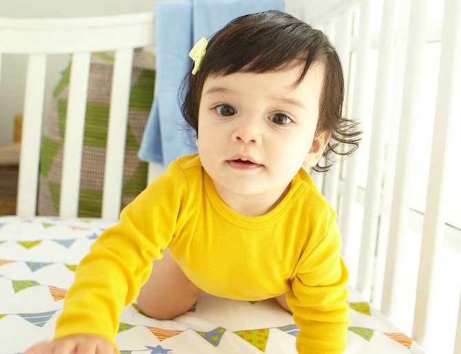Baby in yellow shirt crawling in crib