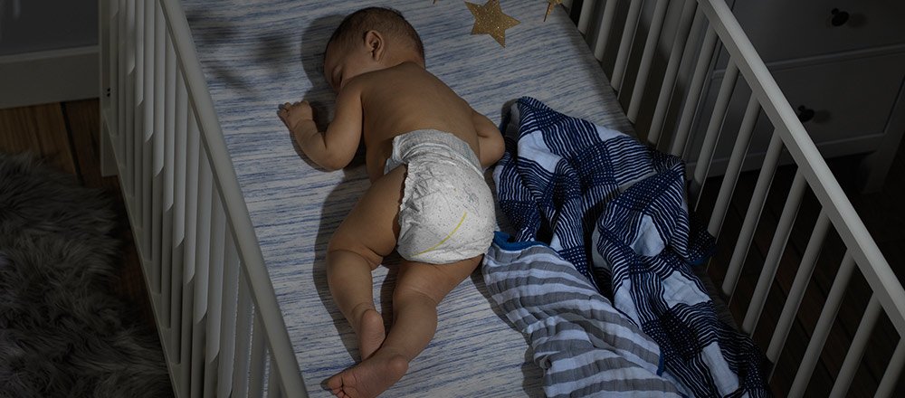 A baby sleeps in a crib wearing a Huggies Overnites Diaper