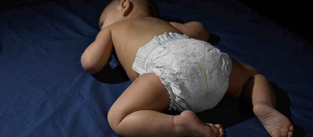 A baby sleeps on their tummy wearing a Huggies Overnites Diaper with extra absorbency