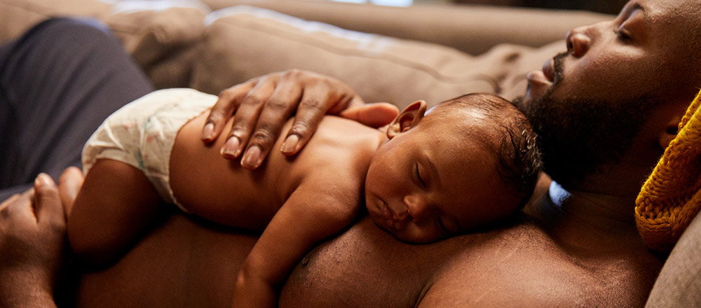 Un bébé portant une couche couché sur la poitrine de son père endormi