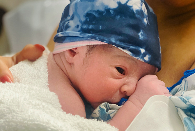 Newborn baby, Adam, laying on his mother's chest with a blue beanie on his head