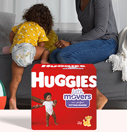 A baby climbs onto a couch next to their mother in front of an image of a box of Huggies Little Movers Diapers