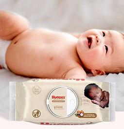 Un bébé portant une couche rit tout en étant couché derrière une image des lingettes Nourish&nbsp;and&nbsp;Care de Huggies