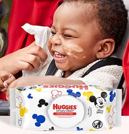 A hand reaches to wipe a laughing baby&#39;s messy face with a Huggies Simply Clean Wipe