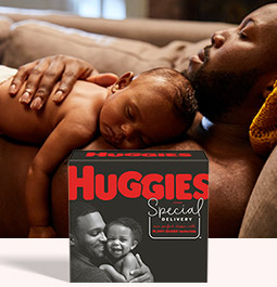 A father lays on a couch while his baby lays on his chest behind an image of Huggies Special Delivery Diapers