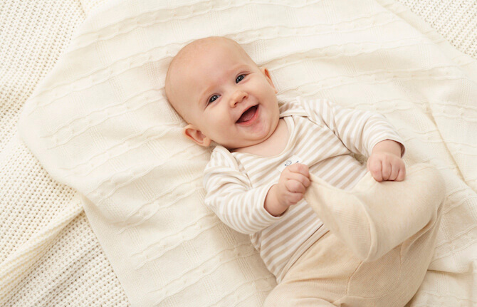 Happy, smiley, baby in white laying on white sheeted bed
