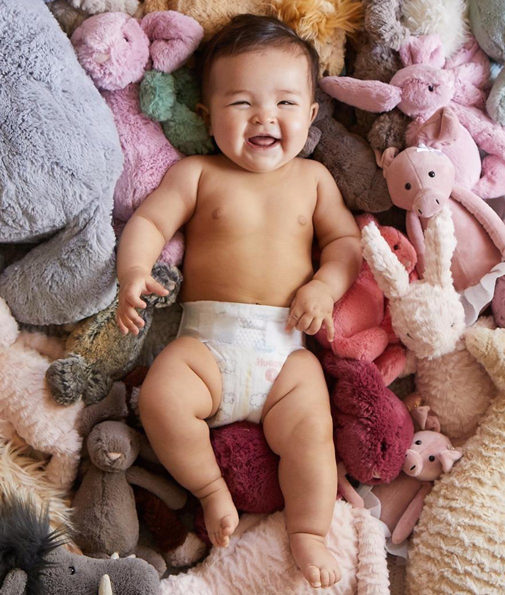 Un bebé riéndose sobre una pila de animales de peluche