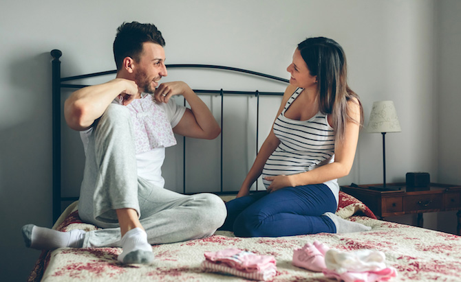 Couple on a bed looking at baby clothes