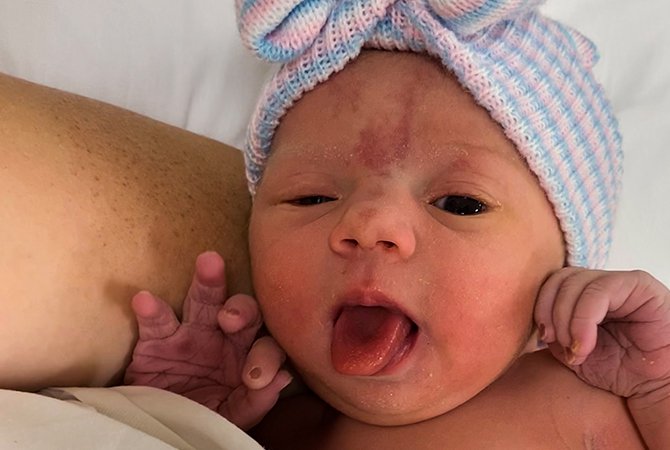 Lana, una bebé recién nacida, saca la lengua con una gorro tejido en la cabeza