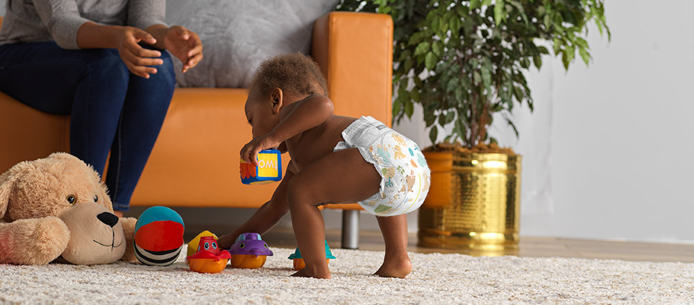 Un bebé en pañales se agacha para levantar juguetes del piso