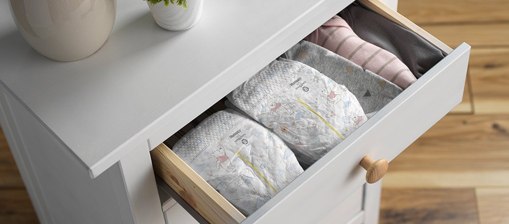 The top drawer of a white dresser is pulled out to display multiple Huggies Little Snugglers Diapers with wetness indicators