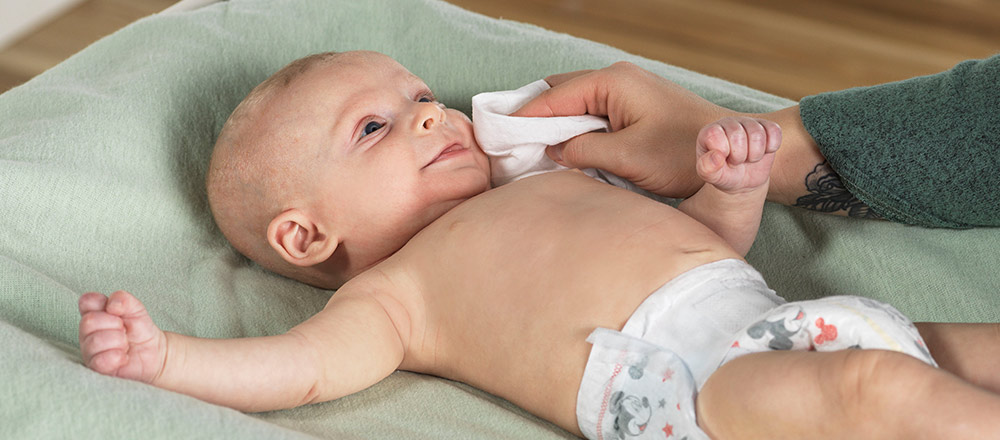 Un parent utilise une lingette pour peau sensible Natural Care de Huggies sur le visage de son bébé couché sur une table à langer