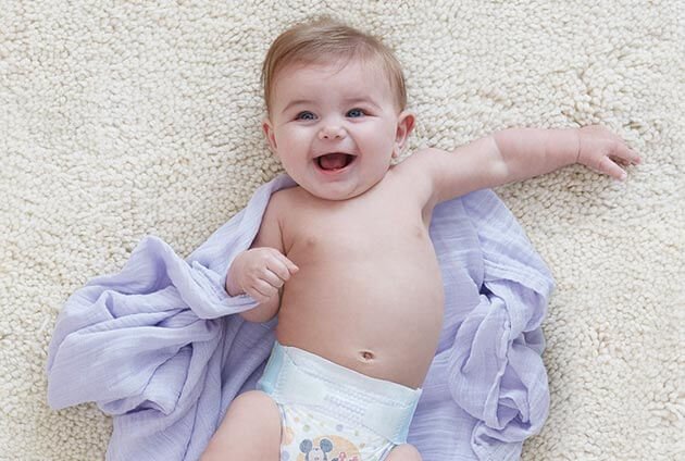 An unswaddled baby laughs while laying on a purple blanket
