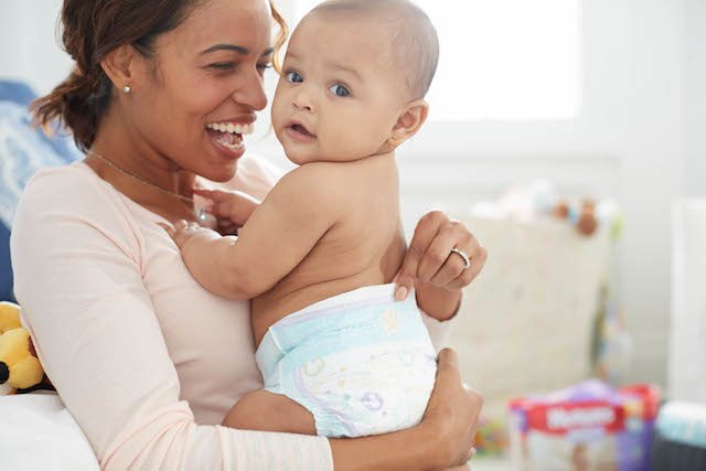 A laughing mother holds her diapered baby that looks at the camera