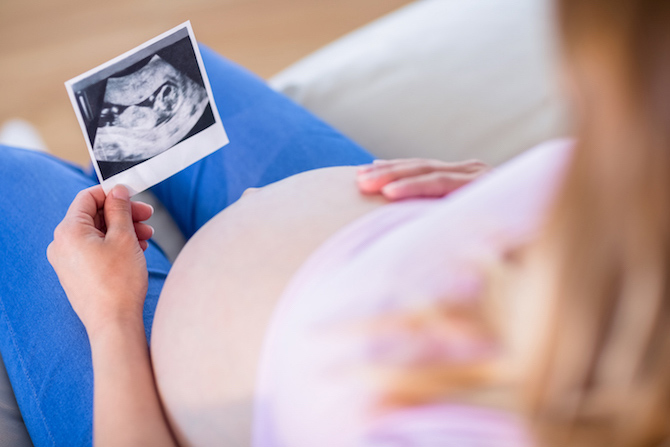 Pregnant lady looking down at Ultra sound picture of what probably is her baby