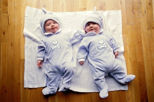 Twin babies in matching onesies laying on a blanket on the floor