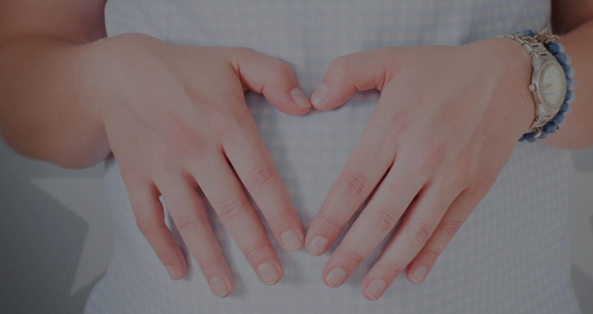 Una mujer embarazada con un reloj apoyando sus manos sobre su estómago en forma de corazón