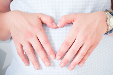 Femme enceinte portant une montre se tient les mains sur le ventre en faisant une forme de c&oelig;ur