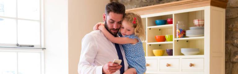 father holding daughter while checking his phone